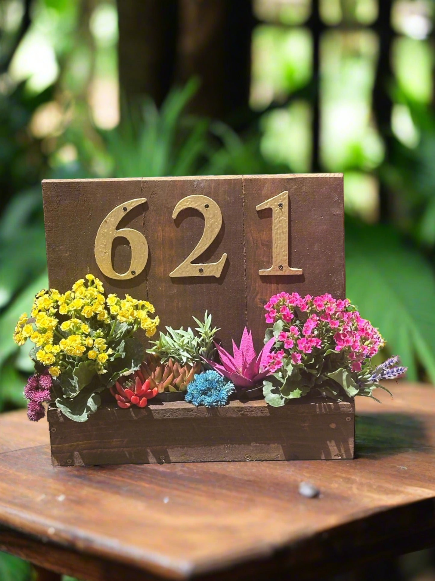 House number planter box displaying "621" in golden numbers, containing vibrant flowers and succulents,  in bright sunlight.